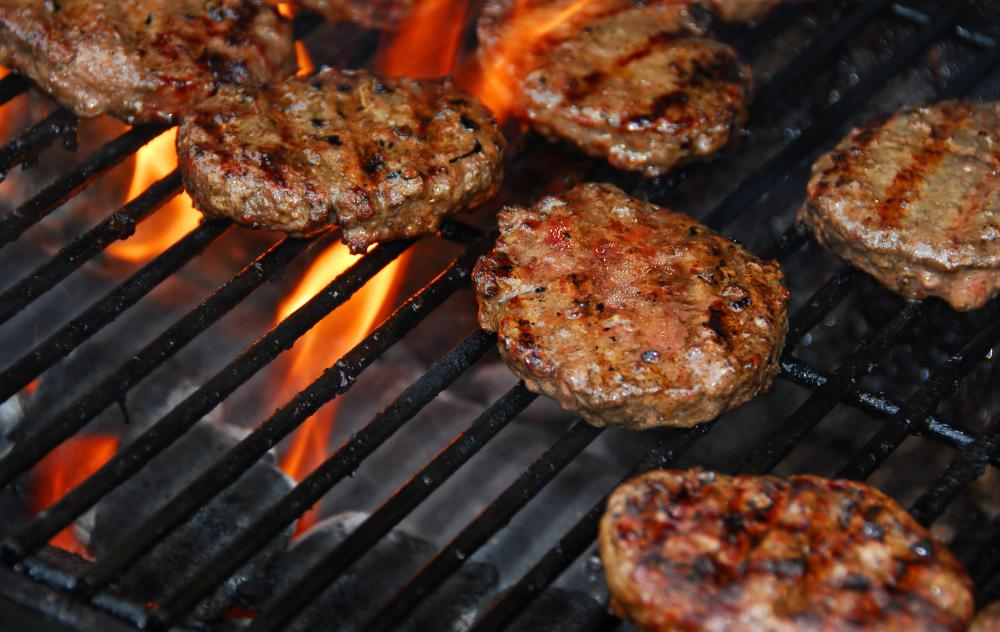 Hamburgers cooking on a grill with charcoal below.
