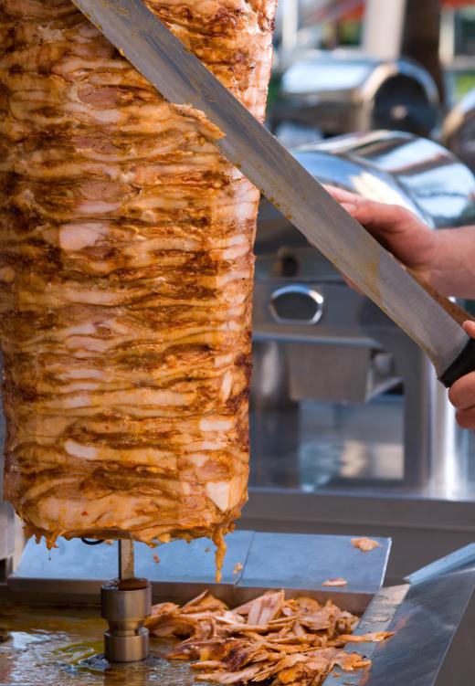 Doner meat for shawarma being cut off the spit with a knife.