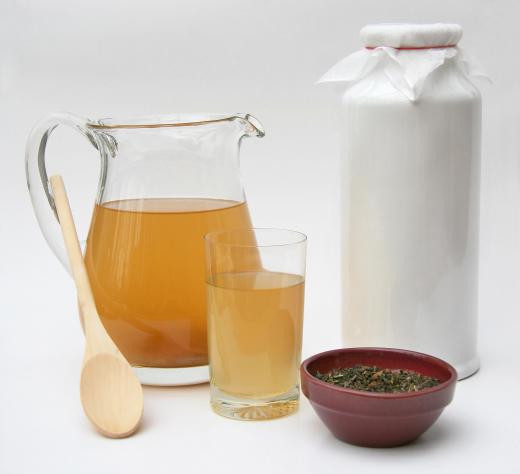 Ingredients for making kombucha tea include green tea, sugar, hot water and a wooden spoon for stirring.